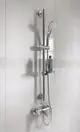 Brausekombination von Ideal Standard mit Halterung, Handbrause und Duschschlauch an heller Wand. Die Ausstattung ist aus verchromtem Material und hat eine einfache, funktionale Form.